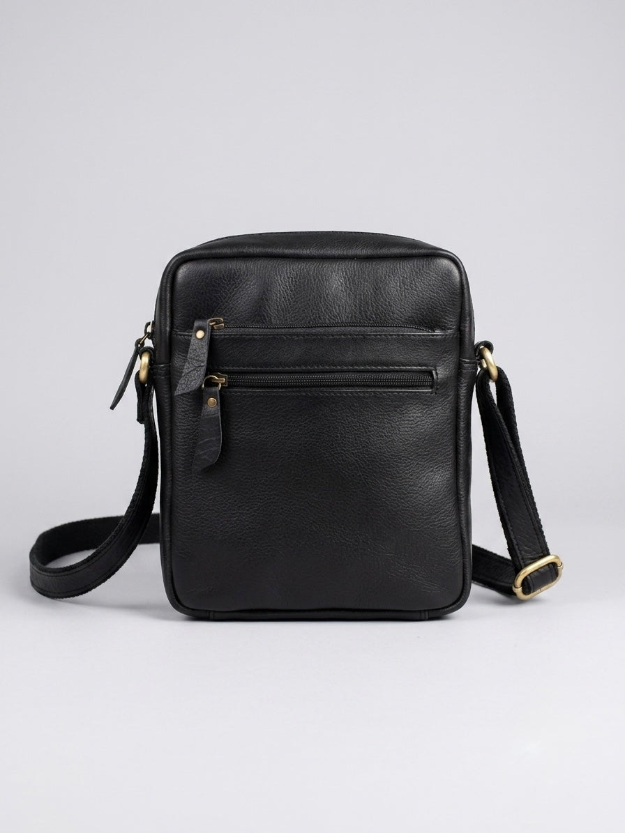 Black leather crossbody bag with a front zip pocket and brass-tone hardware, shown on a light gray background.