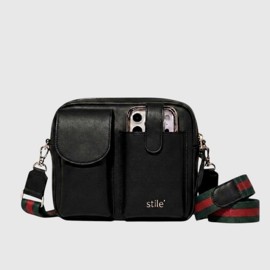 Black genuine leather crossbody phone bag with dual front flap pockets, front slip pocket holding a smartphone, and a green and red striped web-style strap. The brand name 'stile' is printed in gold on the front pocket.