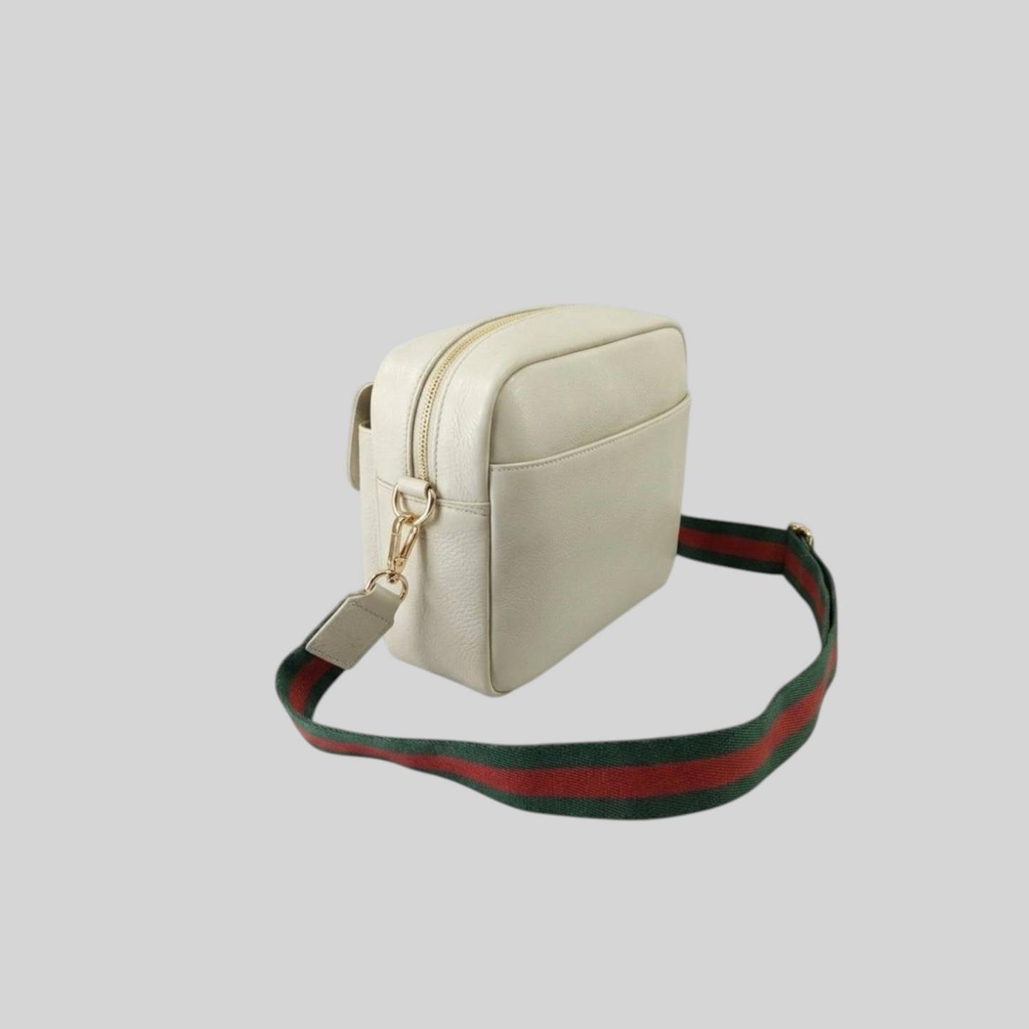 An Ivory genuine leather crossbody bag with a green and red striped web-style shoulder strap and gold-tone hardware, shown on a solid gray background.