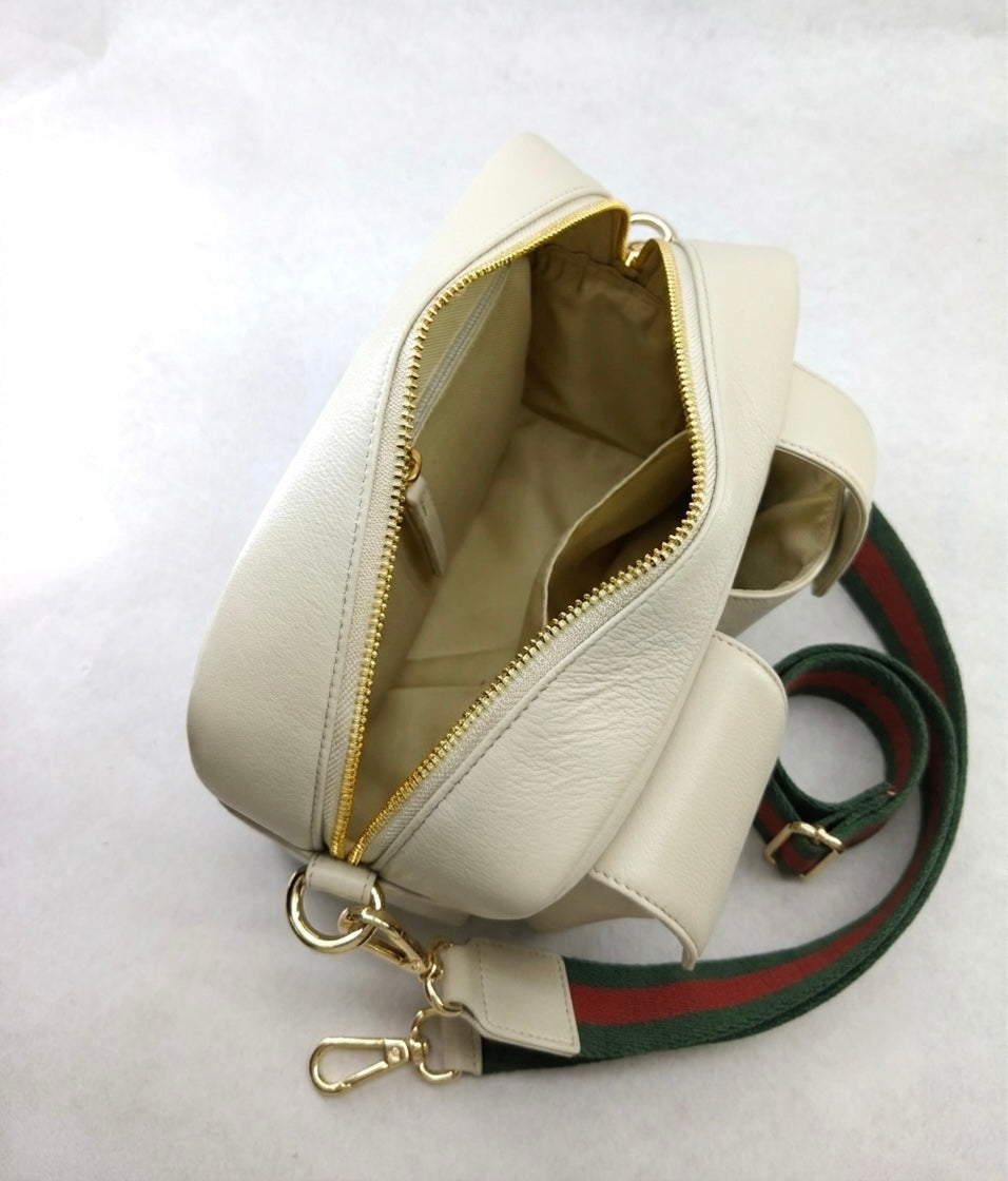 An Ivory leather shoulder bag with gold-tone hardware, shown open to reveal its interior. The bag features a signature green and red web stripe pattern on its strap, set against a light gray background.