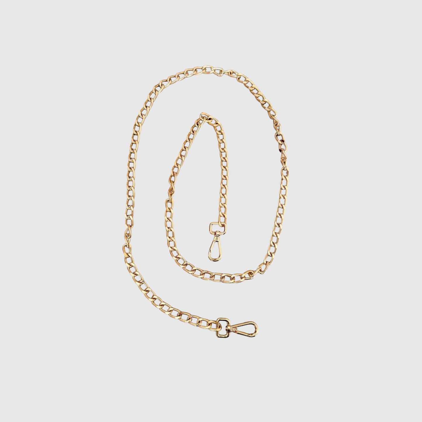 A gold-toned metal chain strap with a clasp arranged on a light gray background.