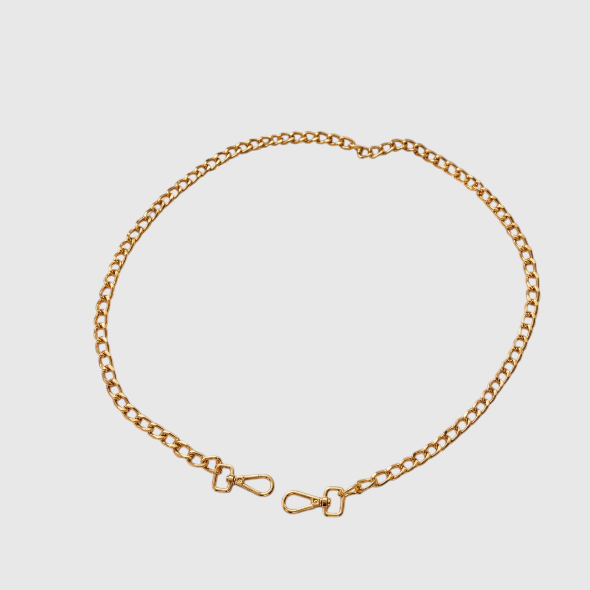 A gold-toned metal chain accessory with clasp ends, arranged in a loose circle on a light gray background.